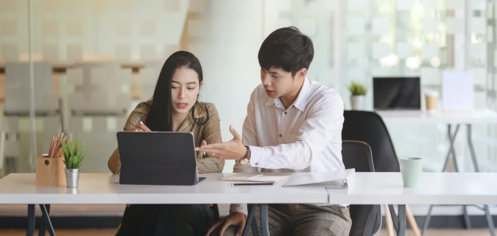 Duas pessoas olham para a tela de um notebook enquanto conversam.