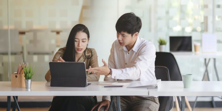 Duas pessoas olham para a tela de um notebook enquanto conversam.